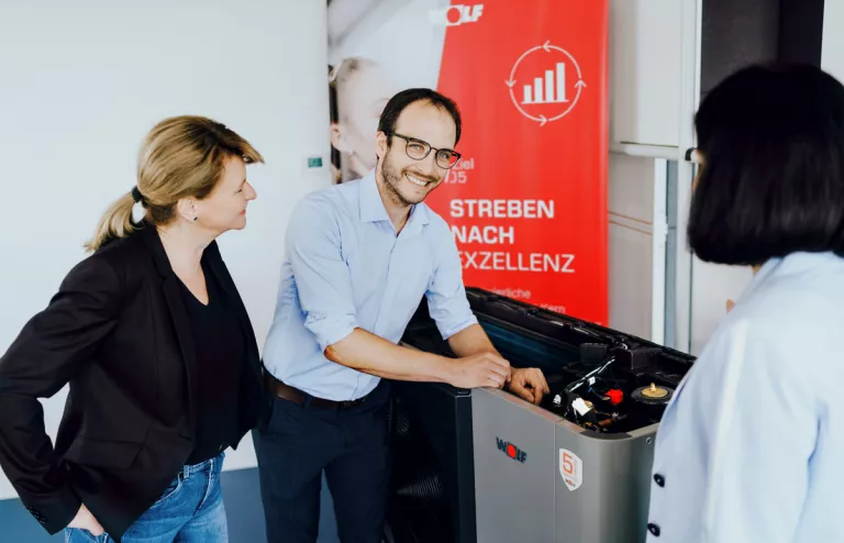 Ein Berater erklärt zwei Damen die Förderungen und Zuschüsse für Wärmepumpen direkt vor einem Gerät.