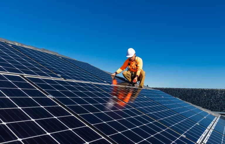 Installateur baut eine große Photovoltaikanlage auf ein Dach bei blauem Himmel.
