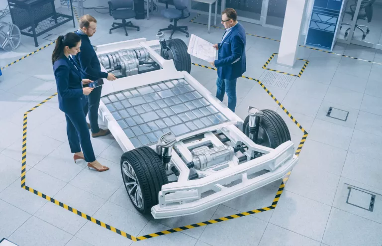 Wissenschaftler stehen um ein Chassis eines Elektroautos herum und begutachten die offen liegenden Batterien, die das E-Auto zu einem mobilen Stromspeicher machen.