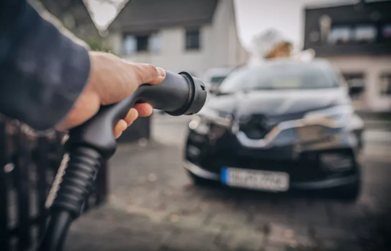 Eine Hand hält eine Ladepistole von einer bidirektionalen Wallbox und bewegt sich auf das Elektroauto zu, um es zu laden.