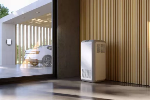 Ein moderner Stromspeicher in einem modernen Raum mit großem Fenster und Blick auf den Carport mit Elektroauto.