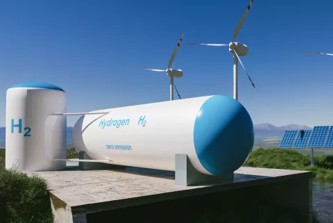 Eine Wasserstoff-Speicher unter freiem Himmel mit Windkrafträdern und Solarmodulen im Hintergrund.