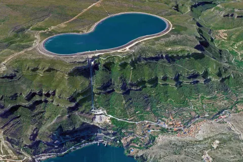 Ein großer See auf einer Hochebene mit einem angeschlossenen Wasser-Kraftwerk und einem Dorf im Tal.