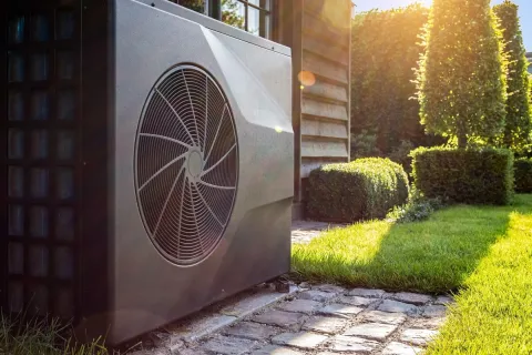 Eine Wärmepumpe vor dem Haus im Hintergrund der Garten.
