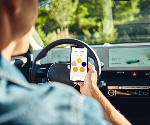 Persona che guida un'auto elettrica ed utilizza l'app SENEC.App con lo smartphone