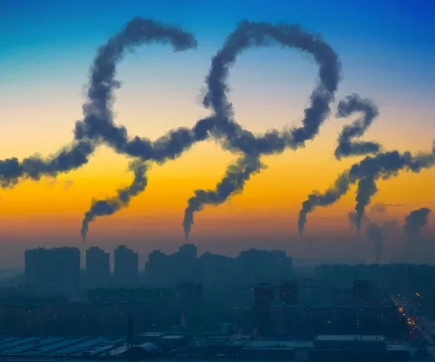 Die Skyline einer Stadt mit aufsteigendem Qualm aus Schornsteinen. Der Qualm zeichnet den Schriftzug CO2 in den Himmel.