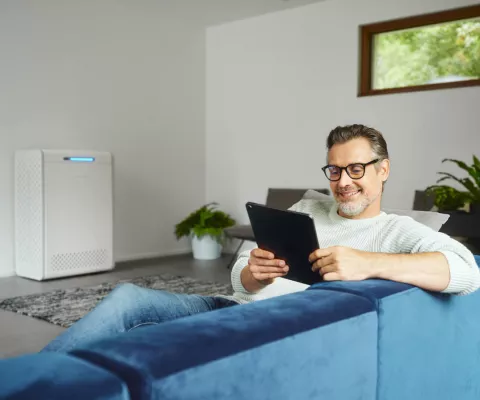 Ein Mann sitzt auf dem Sofa und steuert sein Home Energy Management System per Tablet.