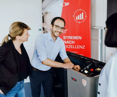 Ein Berater erklärt zwei Damen die Förderungen und Zuschüsse für Wärmepumpen direkt vor einem Gerät.