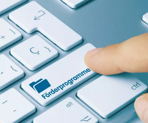 Ein Finger tippt auf der Tastatur auf eine Taste mit der Aufschrift Förderprogramme.