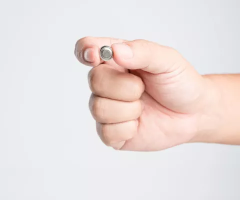 Eine Hand hält eine ganz kleine Batterie zwischen den Fingern.